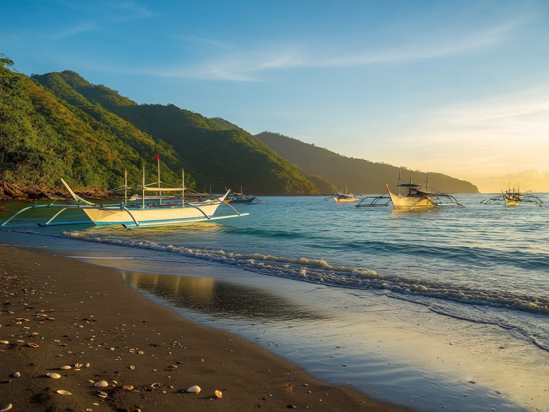 Traditional wooden fishing boats on a tropical beach during sunset, with lush green mountains and calm ocean waves in the background.