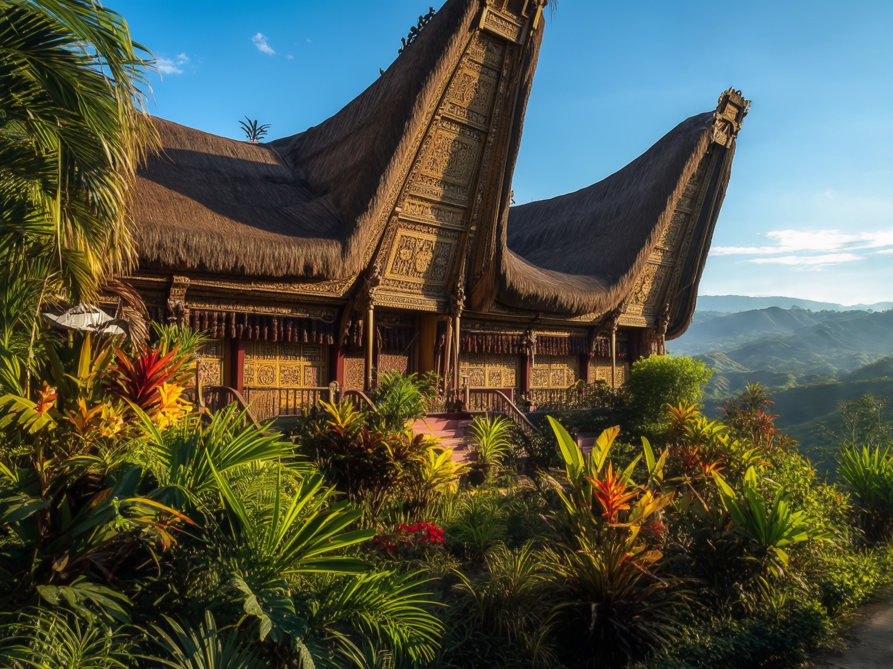 Traditional Indonesian house with ornate carvings and thatched roof, surrounded by lush tropical plants and scenic mountain views in the background.