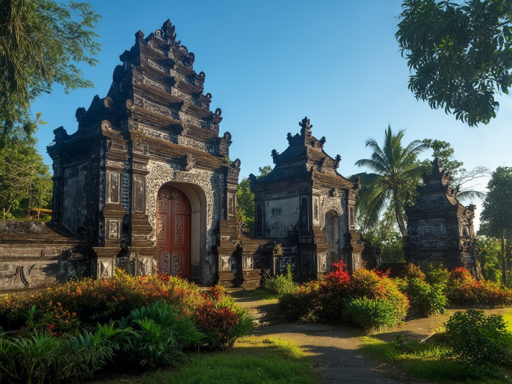 Traditional Balinese temple gate amidst lush tropical plants and bright sunlight against a clear blue sky.