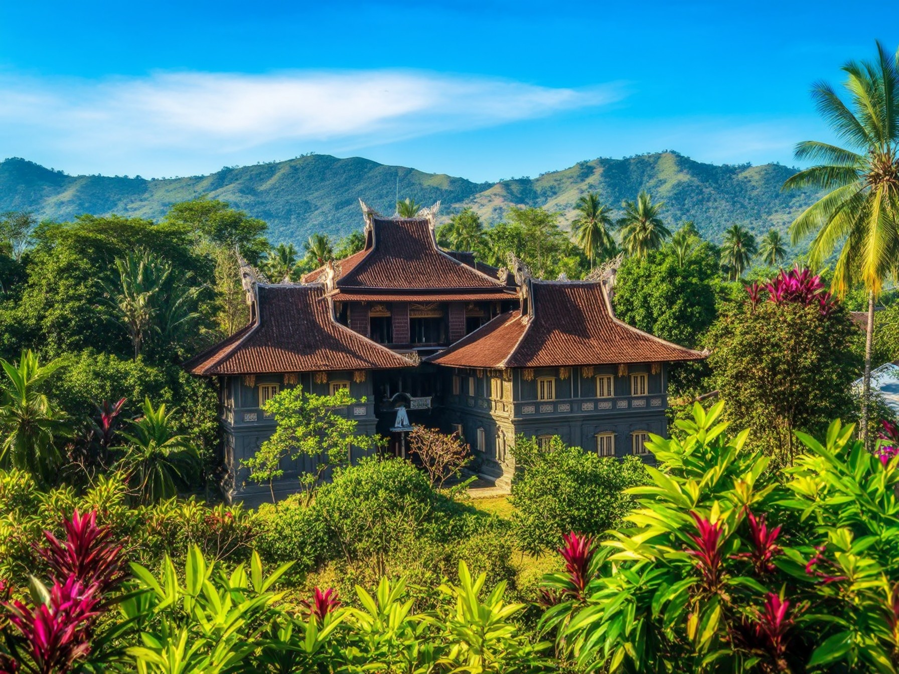 A traditional Asian-style building surrounded by lush tropical greenery and mountains under a clear blue sky.