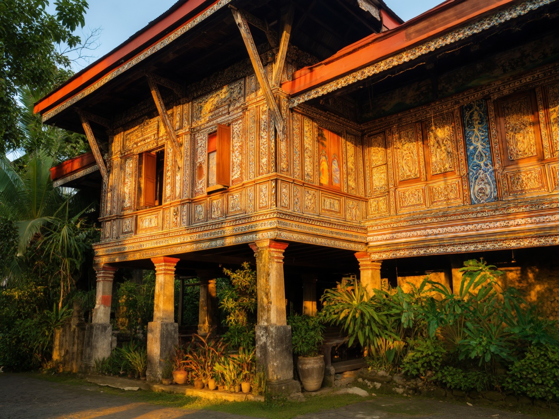 Traditional wooden house in Phuket with intricate carvings and lush greenery at sunset.